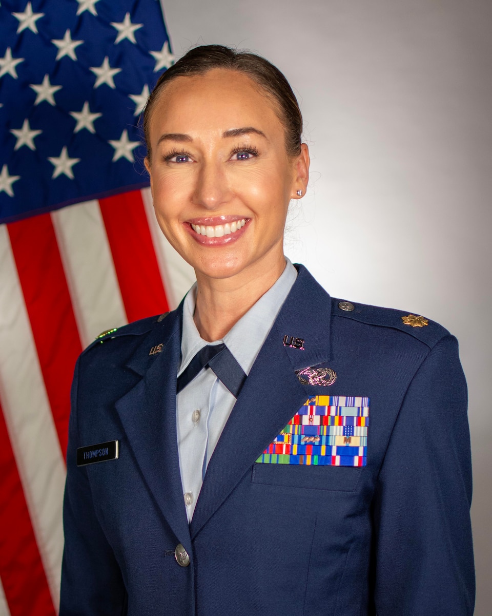 Service member smiles for official portrait in front of US flag wearing their service dress