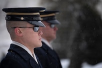 Two Army Soldiers wearing sunglasses and ceremonial hats are standing next to each other facing towards the right.