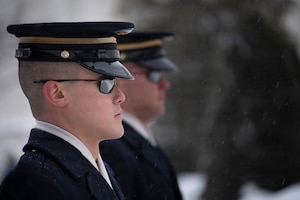 Two Army Soldiers wearing sunglasses and ceremonial hats are standing next to each other facing towards the right.