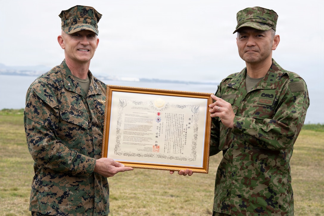 U.S. Marine Corps Brig. Gen. Robert Brodie, left, the offgoing commanding general of 3rd Marine Expeditionary Brigade, holds his award citation for the Japan Defense Cooperation Medal with Japan Ground Self-Defense Force Maj. Gen. Toshikatsu Musha, commanding general of the JGSDF Amphibious Rapid Deployment Brigade, Camp Courtney, Okinawa, Japan, Feb. 6, 2026. Brig. Gen. Robert Brodie received this award in honor of his dedicated and faithful service to strengthen the alliance between the U.S. and Japan while acting as the commanding general of 3rd MEB. He was awarded upon the completion of the 3rd MEB change of command ceremony. 3rd MEB hosted the change of command ceremony to formally recognize the total transfer of authority from Brig. Gen. Robert Brodie to Brig. Gen. Ryan Hoyle. The unit conducts combined operations, exercises, and training in support of the III Marine Expeditionary Force to strengthen alliance relationships and enhance regional security. (U.S. Marine Corps photo by Staff Sgt. Shannon Doherty)