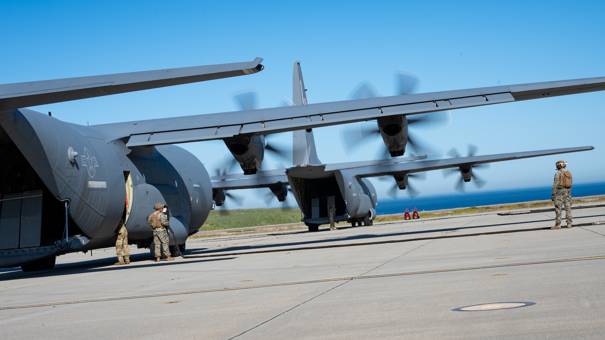 Two U.S. Air Force C-130J Super Hercules assigned to the 19th Airlift Wing and 317th Airlift Wing remain running while U.S. Marines assigned to Marine Wing Support Squadron 372 prepare fuel lines during Specialized Fueling Operations at Naval Landing Field, San Clemente Island, California, Feb. 4, 2026. The training validated repeatable joint fueling procedures in support of distributed operations during the Spring 2026 C-130 Weapon System Council led by the 317th AW. (U.S. Air Force photo by Senior Airman Jade M. Caldwell)