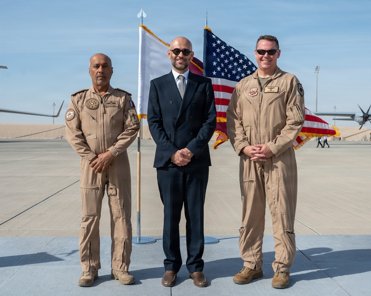 Qatar Emiri Air Force Staff Col. Pilot Mubarak Hasan Albin Ali, Al Udeid Air Base commander, Mo Barghouty, U.S. Embassy Doha Chargé d’Affaires, and U.S. Air Force Brig. Gen. Daniel Clayton stand together on a stage with Qatar and U.S. flags flyying behind them.