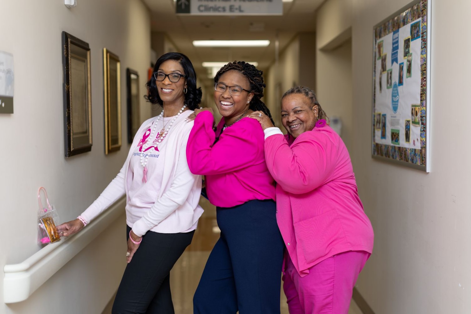 Three women in pink clothes smile together in a hallway