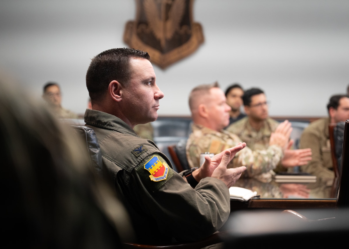 A Colonel in an Air Force flight suit is clapping as he is watching the space in front of him. There are several other people clapping around him, all in Air Force OCP uniforms.