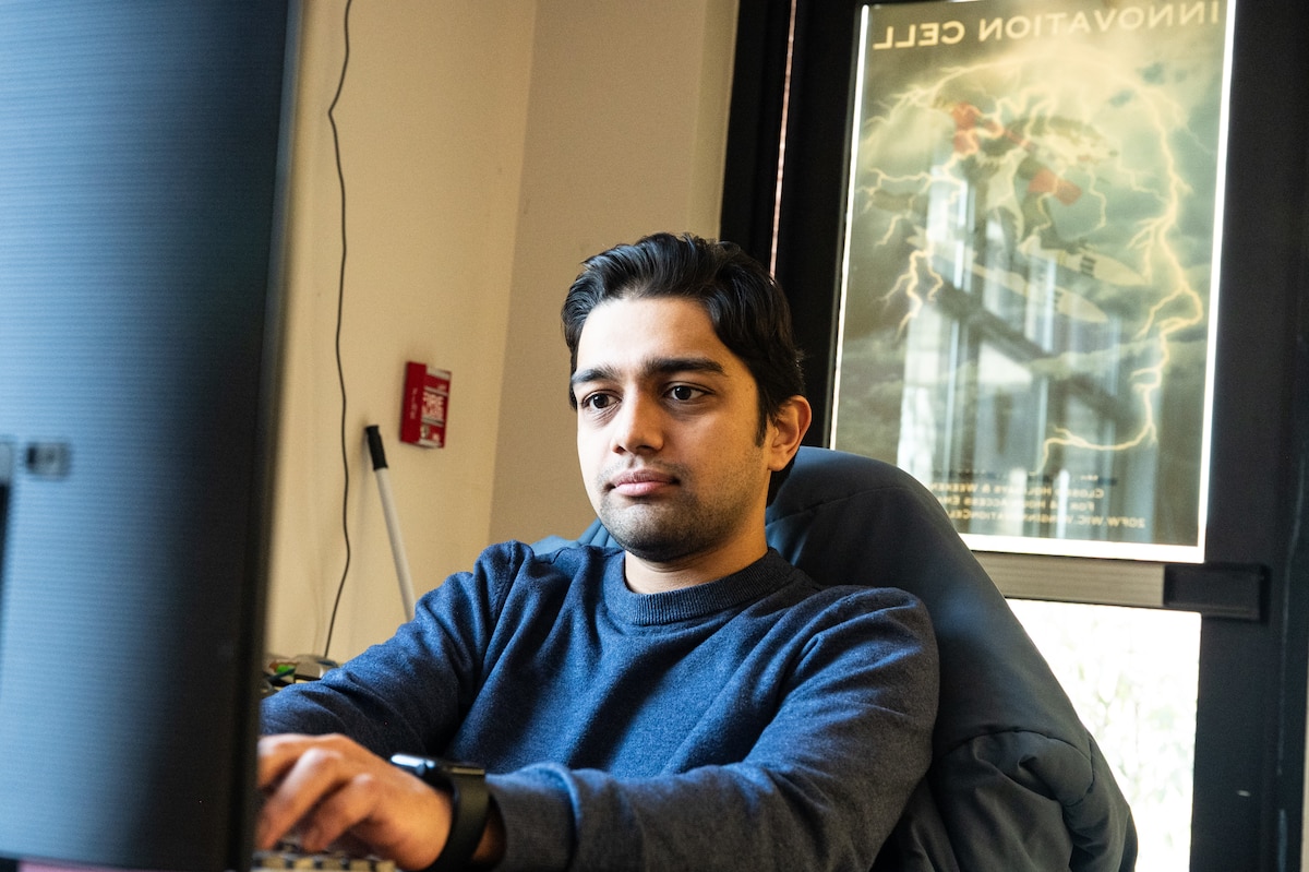 A man sits in front of a computer with his eyes on the screen and his hands on the keyboard. There is a door behind him that reads "Innovation Cell".