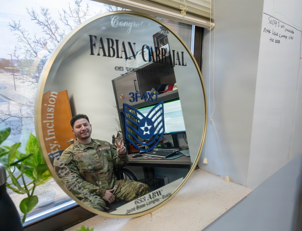 U.S. Airman sits at a desk smiling into a mirror.
