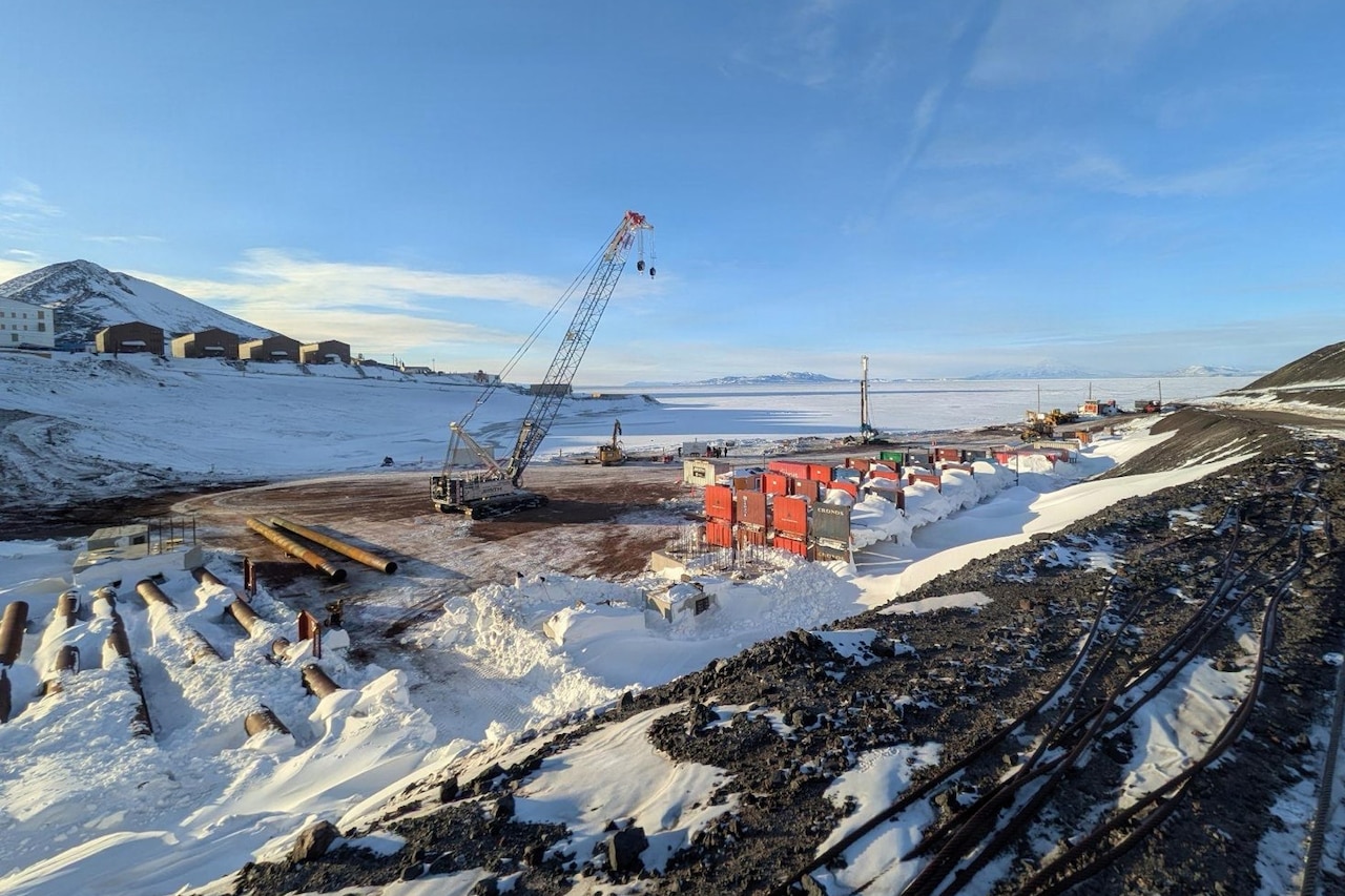 A crane and several other pieces of construction equipment work on a storage facility in a snowy landscape.