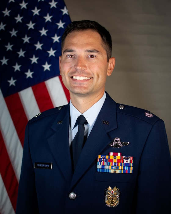 Service member smiles for official portrait in front of US flag wearing their service dress blues