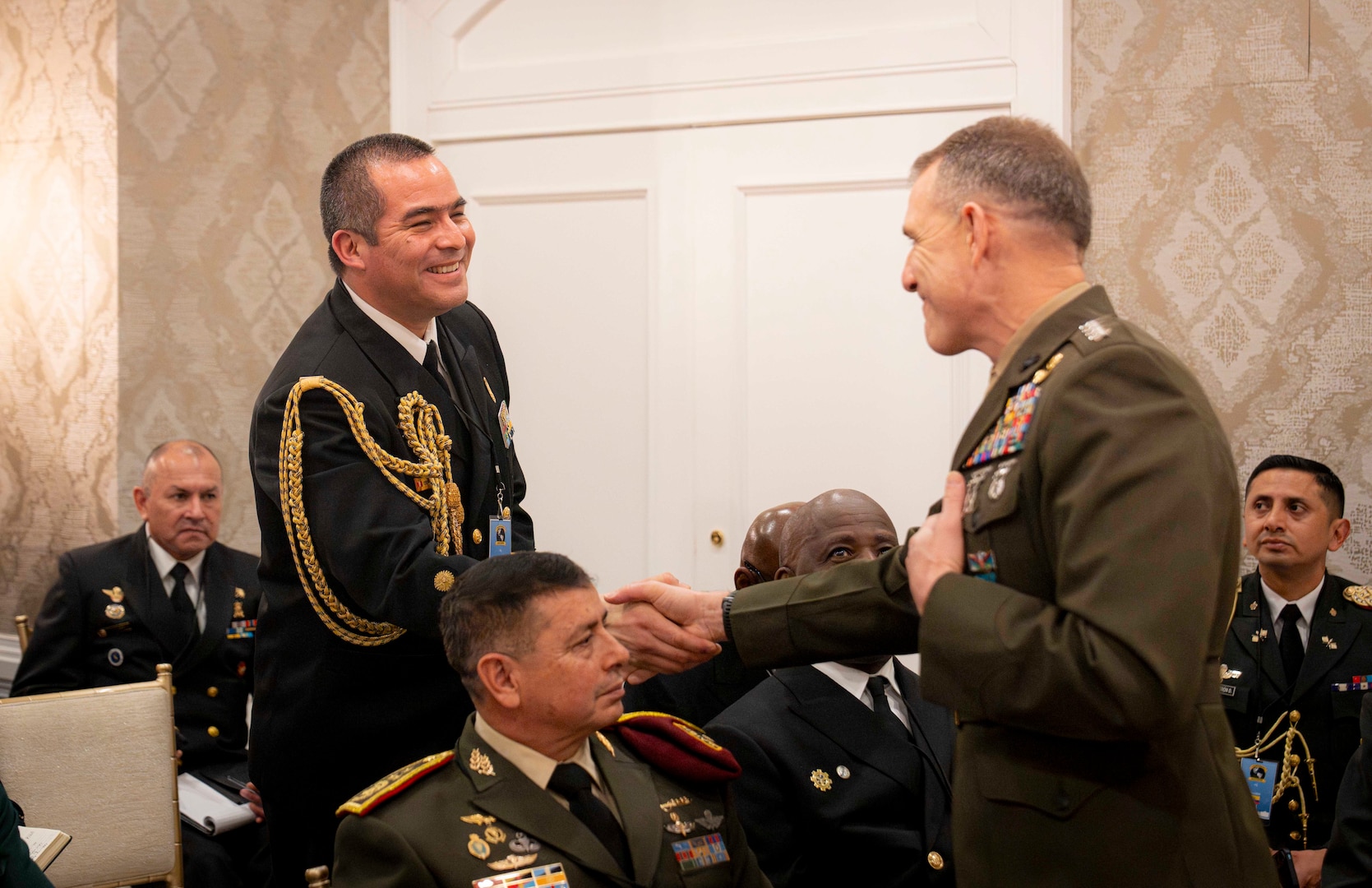 Two men in dress military unforms shake hands.