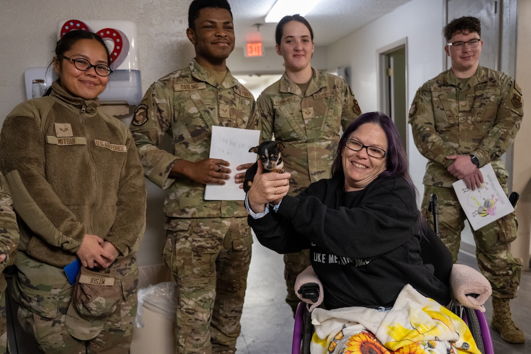 U.S. Air Force Airmen assigned to the 97th Air Mobility Wing smile with a veteran and her dog at English Village Manor in Altus, Oklahoma, Feb. 10, 2026. The interaction supported a volunteer outreach event called Valentines for Vets focused on spreading encouragement to veterans throughout the local community. (U.S. Air Force photo by Airman 1st Class Nathan Langston)