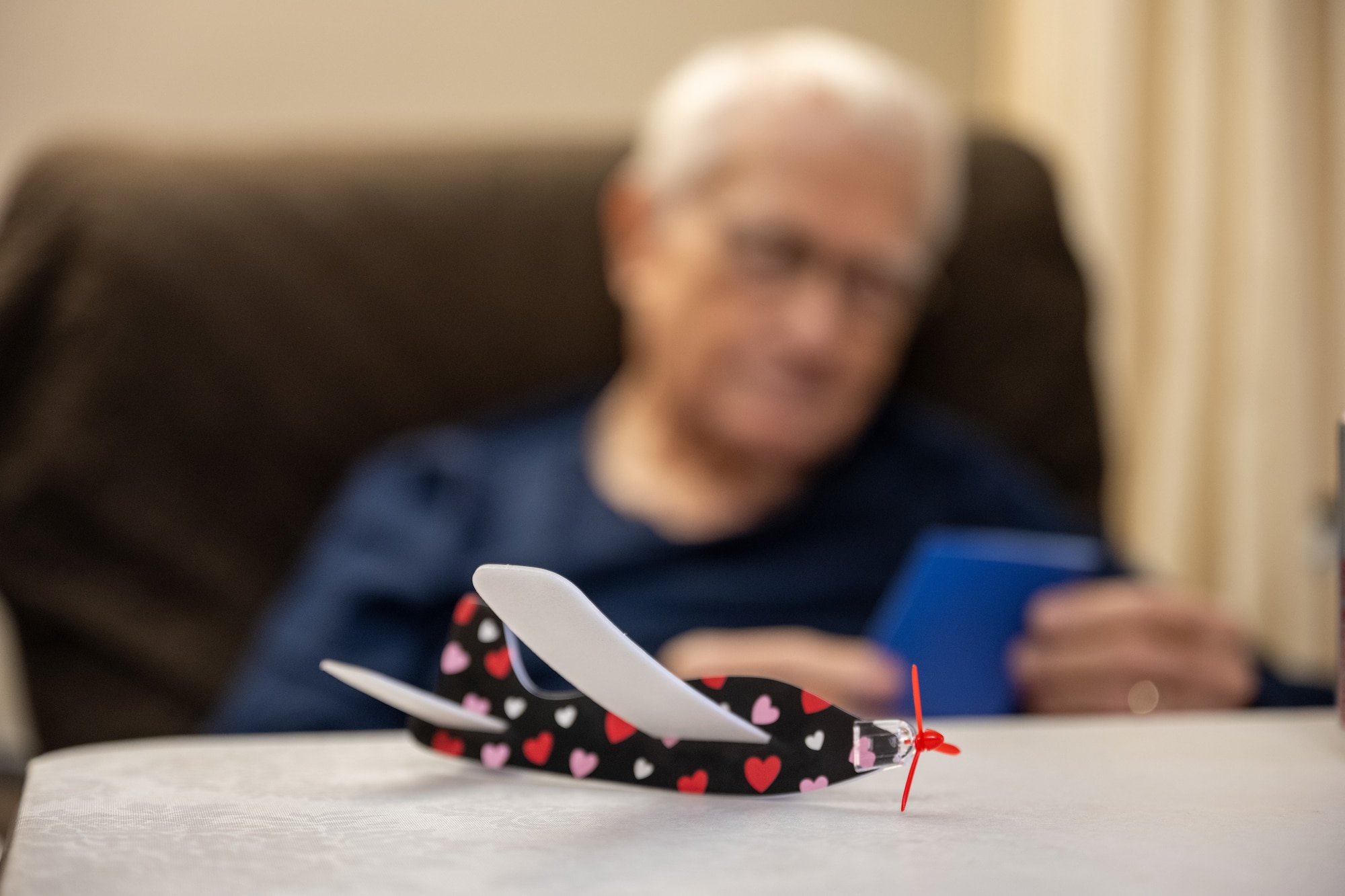 A veteran sits with a gifted valentine’s themed paper plane at The Courtyards at Magnolia in Altus, Oklahoma, Feb. 10, 2026. The gift was delivered by U.S. Air Force Airmen as part of a volunteer outreach event to share messages of appreciation with local veterans. (U.S. Air Force photo by Airman 1st Class Nathan Langston)