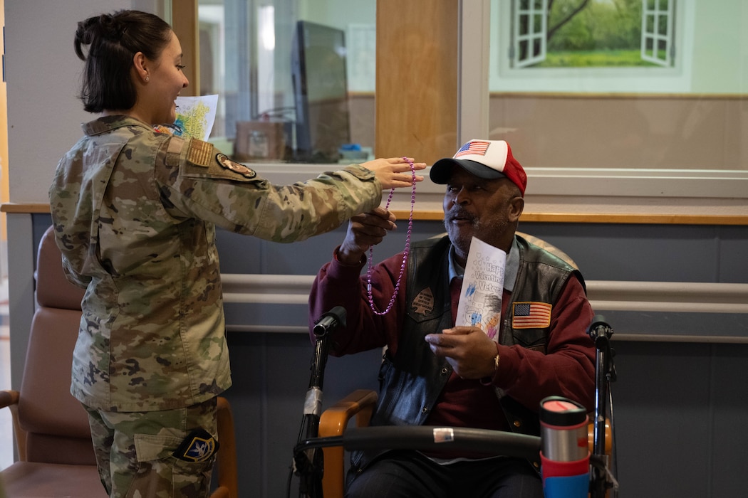 U.S. Air Force Senior Airman Jaeleen Bell-Acurero, 97th Security Forces Squadron unit scheduler, hands a necklace and a valentine to a veteran at Clinton Veterans Home in Clinton, Oklahoma, Feb. 10, 2026. Bell-Acurero was one of the Airmen from Altus Air Force Base that took part in delivering valentines to veterans at nearby assisted living facilities. (U.S. Air Force photo by Airman 1st Class Emma Wright)