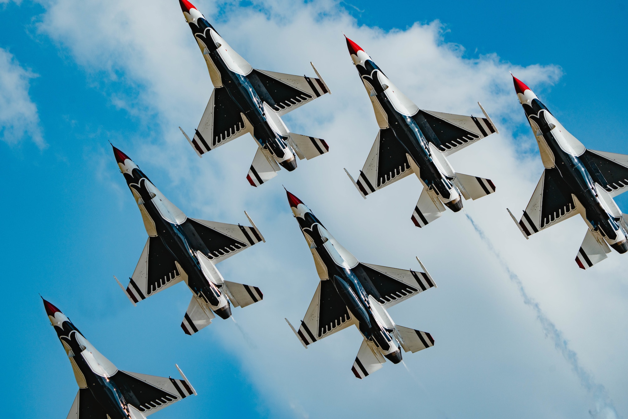 Fighter jet formation flying in front of a blue sky with clouds
