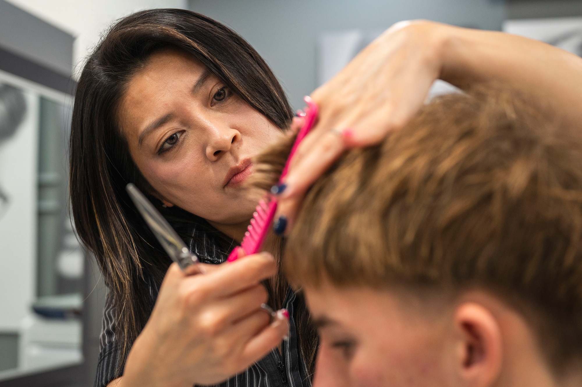 Ayu Uehara, Kadena Air Base Exchange hair stylist, cuts a client’s hair at the Kadena AB Exchange, Japan, Jan. 8, 2026. By serving 70–100 customers daily, the salon directly supports the daily operations and well-being of the Kadena community, allowing Airmen to remain mission-ready. (U.S. Air Force photo by Senior Airman James Johnson)