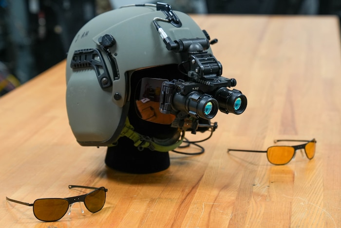 two pairs of eyewear sit on a table next to a mannequin wearing night vision goggles with peripheral protection and a helmet