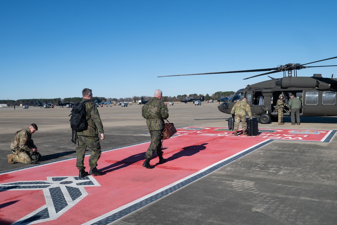 Military members walk down red walkway on flightline towards helicopter
