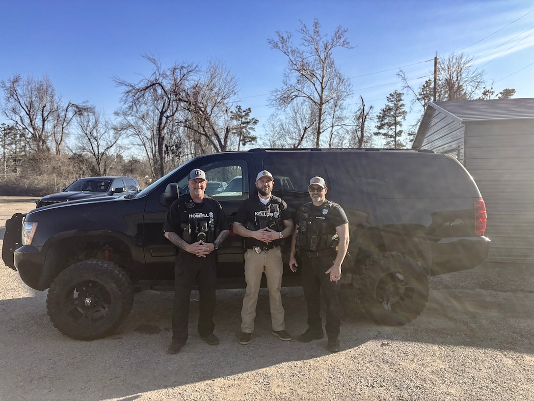 Three Police officers stand next to a black SUV outside
