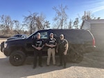 Three Police officers stand next to a black SUV outside