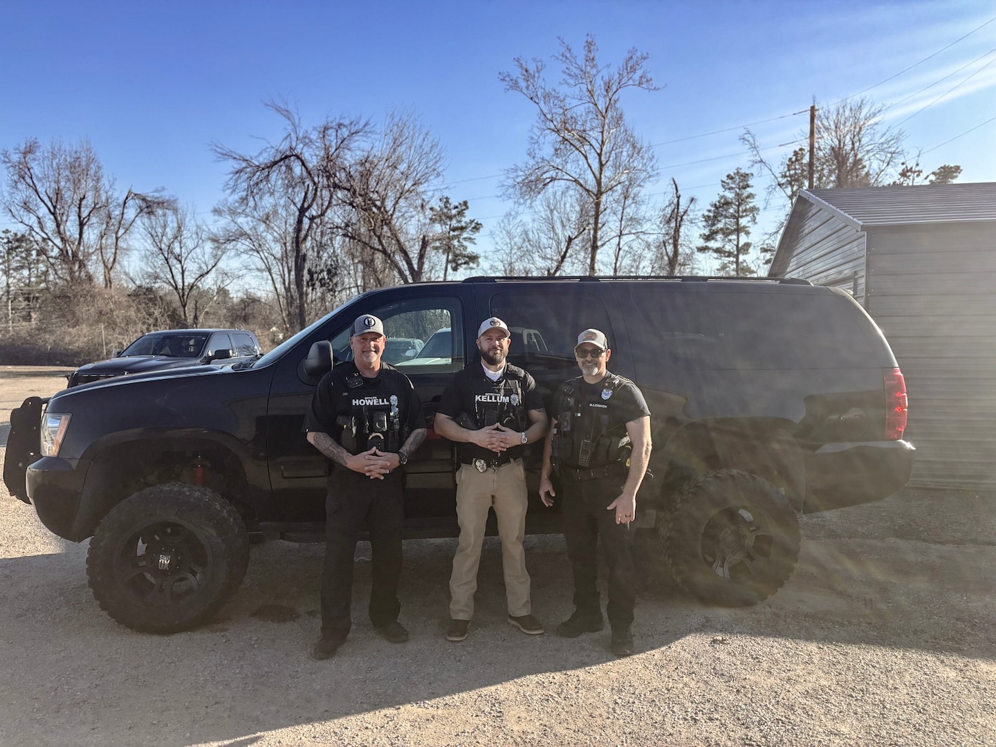 Three Police officers stand next to a black SUV outside