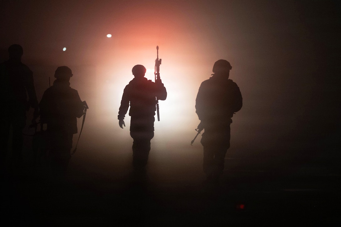 Silhouettes of four people holding weapons are seen, with a white glow behind them.