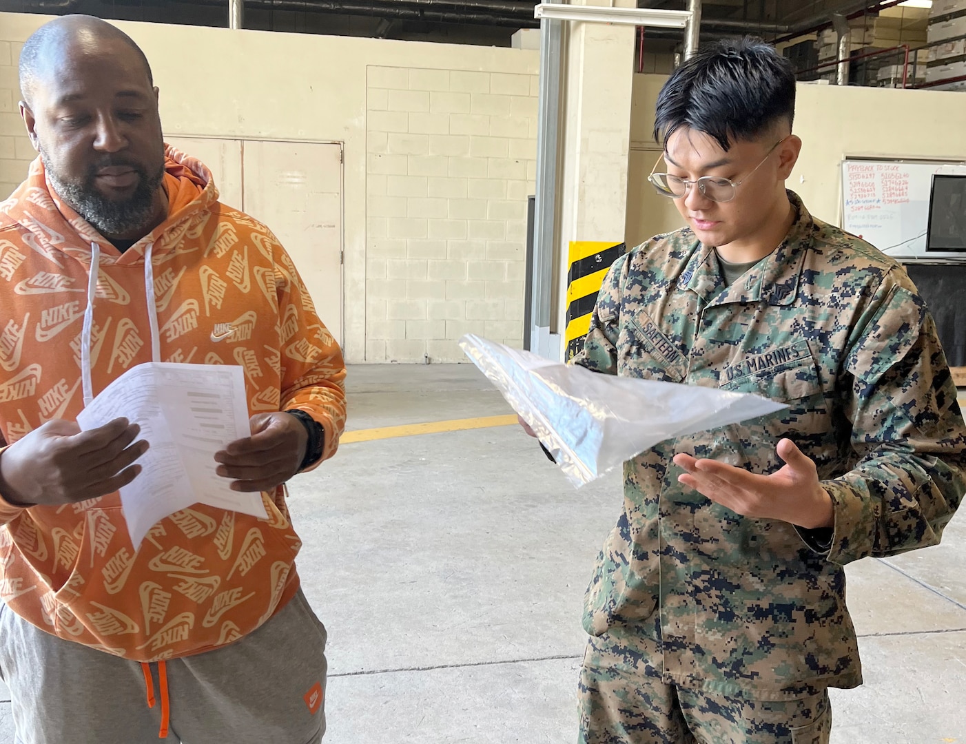 A man in civilian clothes reviews a form after turning over repair parts to a male Marine.