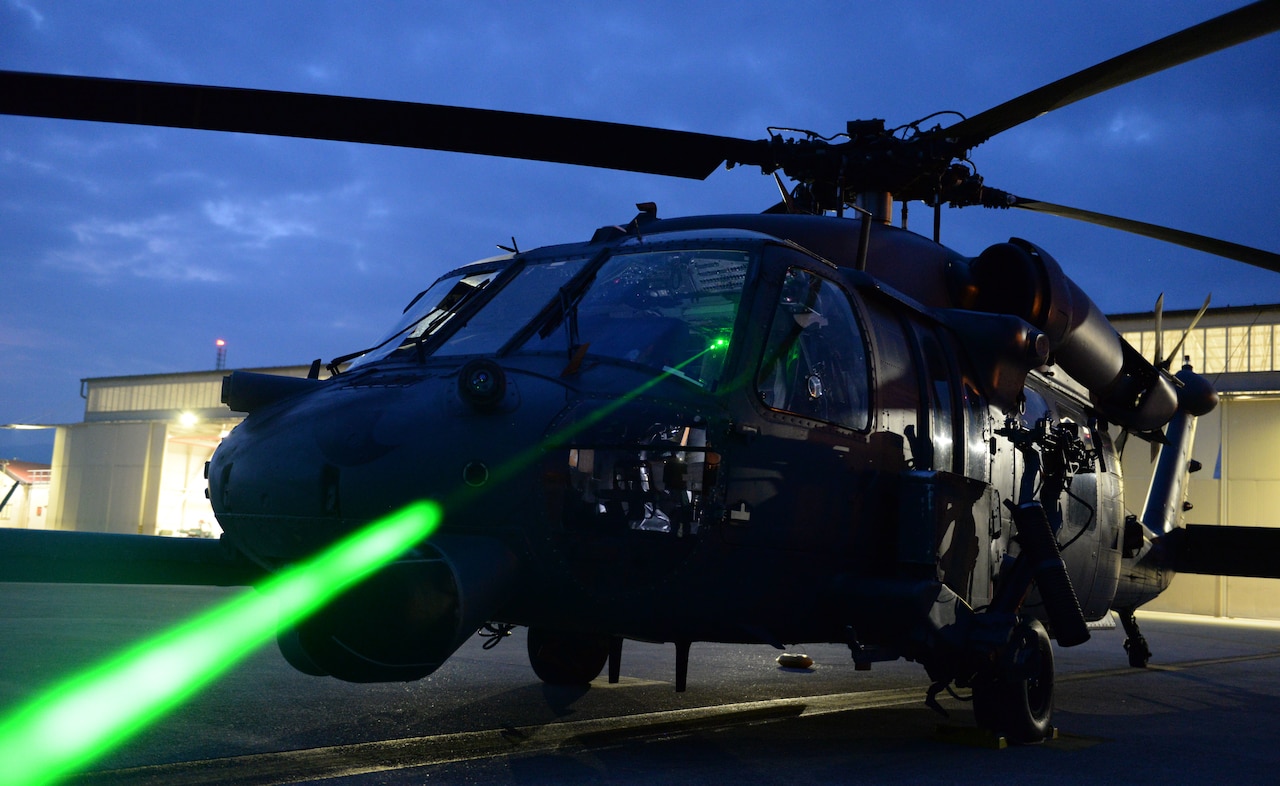 A green laser light beam shines from the cockpit of a helicopter.