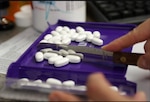 Pharmacist sorts pills with tool.