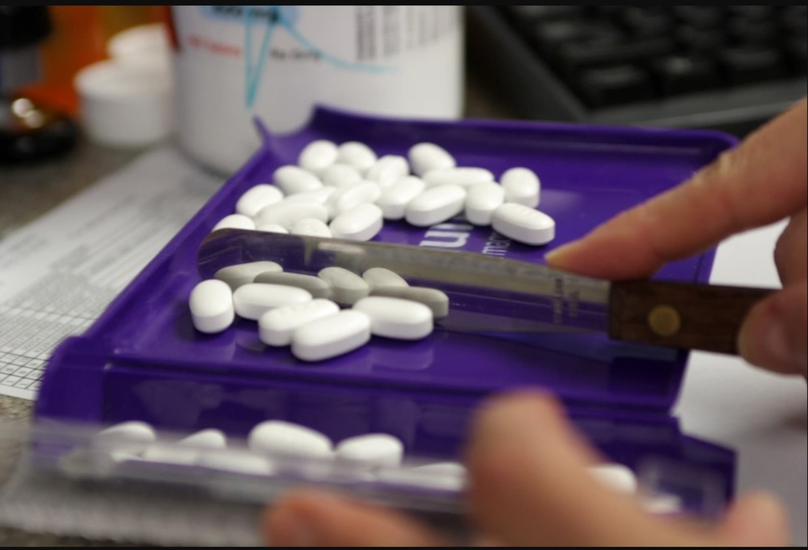 Pharmacist sorts pills with tool.