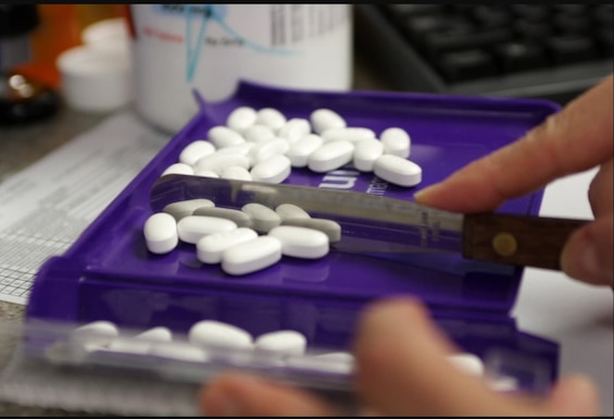 Pharmacist sorts pills with tool.