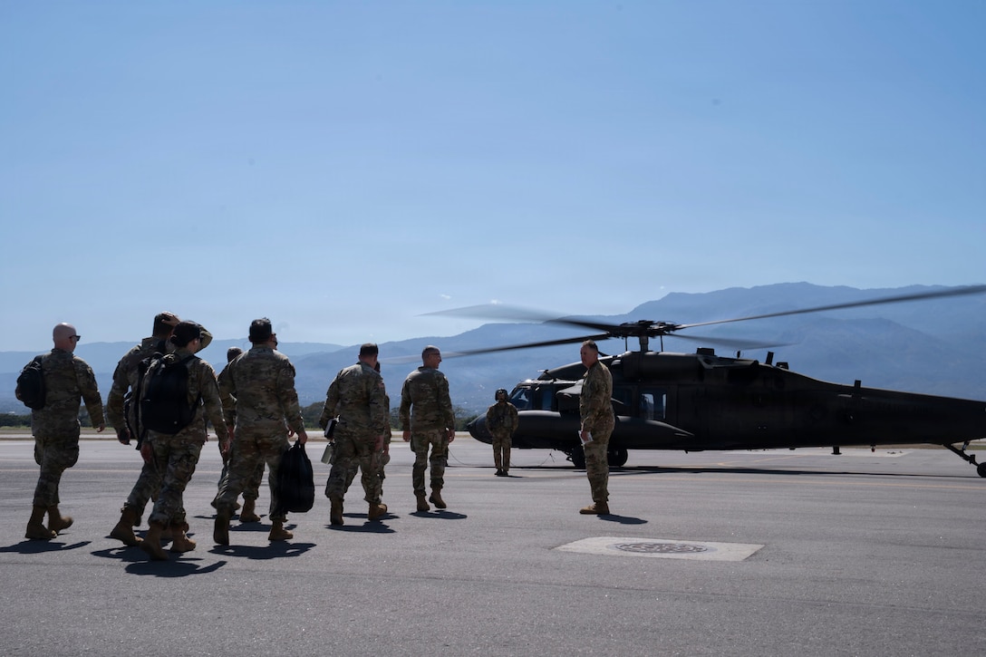 People in military uniforms walk towards a military helicopter