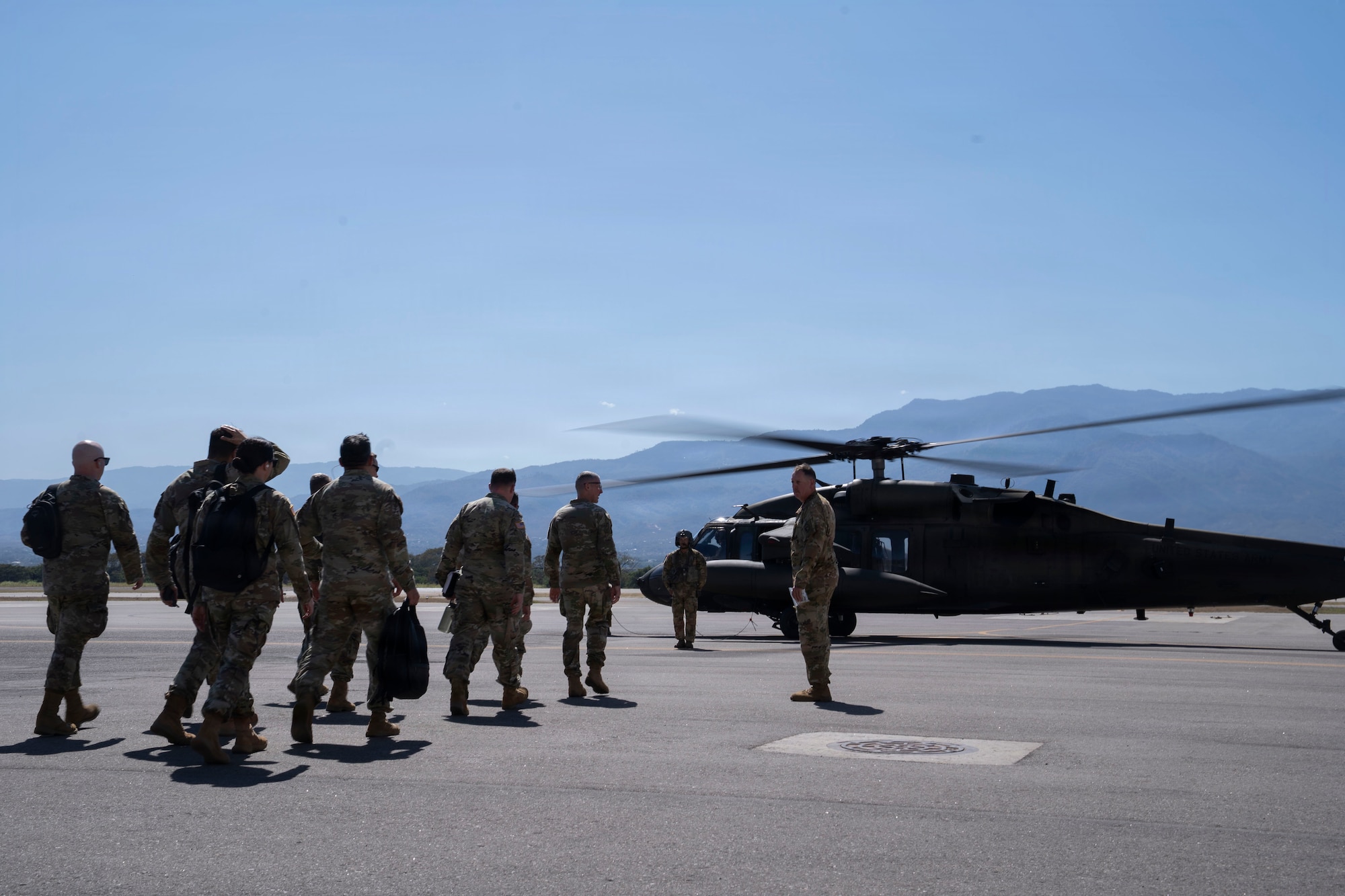 People in military uniforms walk towards a military helicopter