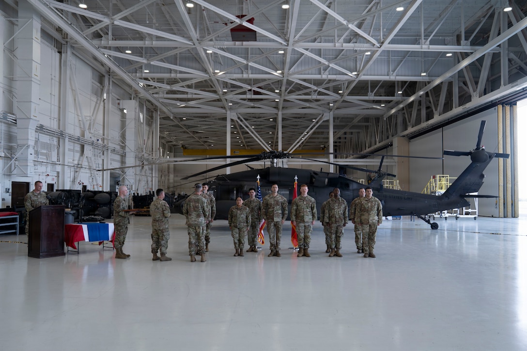 Military members line up in formation in front of a helicopter