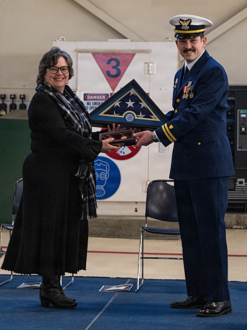 Lt. Jakob Daubert, commanding officer of Coast Guard Cutter Frederick Mann (WPC 1160), presents challenge coins and a national flag to the cutter’s sponsor and niece of Frederick Mann, Mrs. Eugenia “Jeannie” Mann Hyder, during the cutter’s commissioning ceremony at Coast Guard Base Kodiak, Alaska, Feb. 13, 2026. The commissioning solidified the Mann as the sixth fast response cutter to be homeported in Alaska, and it was presided over by Rear Adm. Bob Little, commander of the Coast Guard’s Arctic District. (U.S. Coast Guard photo by Petty Officer 3rd Class Cameron Snell)