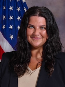 Elise Annett poses facing the camera with the U.S. flag in the background.