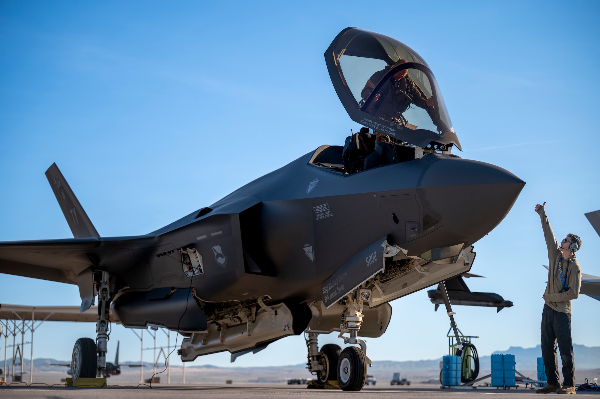 a maintainer signals a pilot next a fighter jet