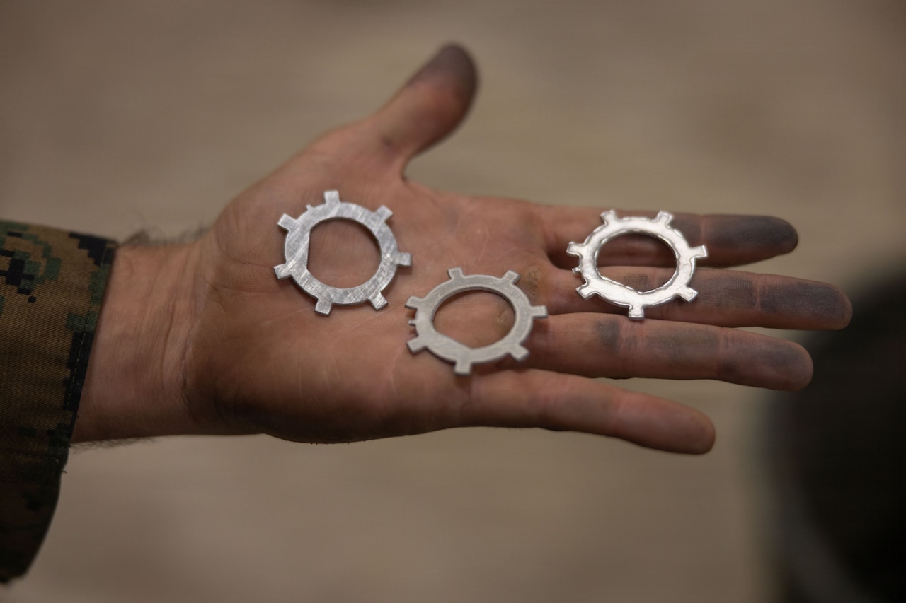 A close-up of a dirty hand holding three metal washers.