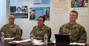 Three Airmen sit at a table during a town hall discussion.
