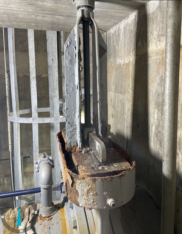 A metal component with orange and brown rust with concrete walls in the background.