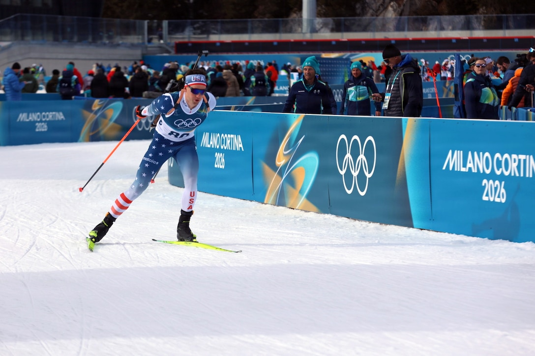 A soldier skis during a competition as spectators watch from behind a barrier.