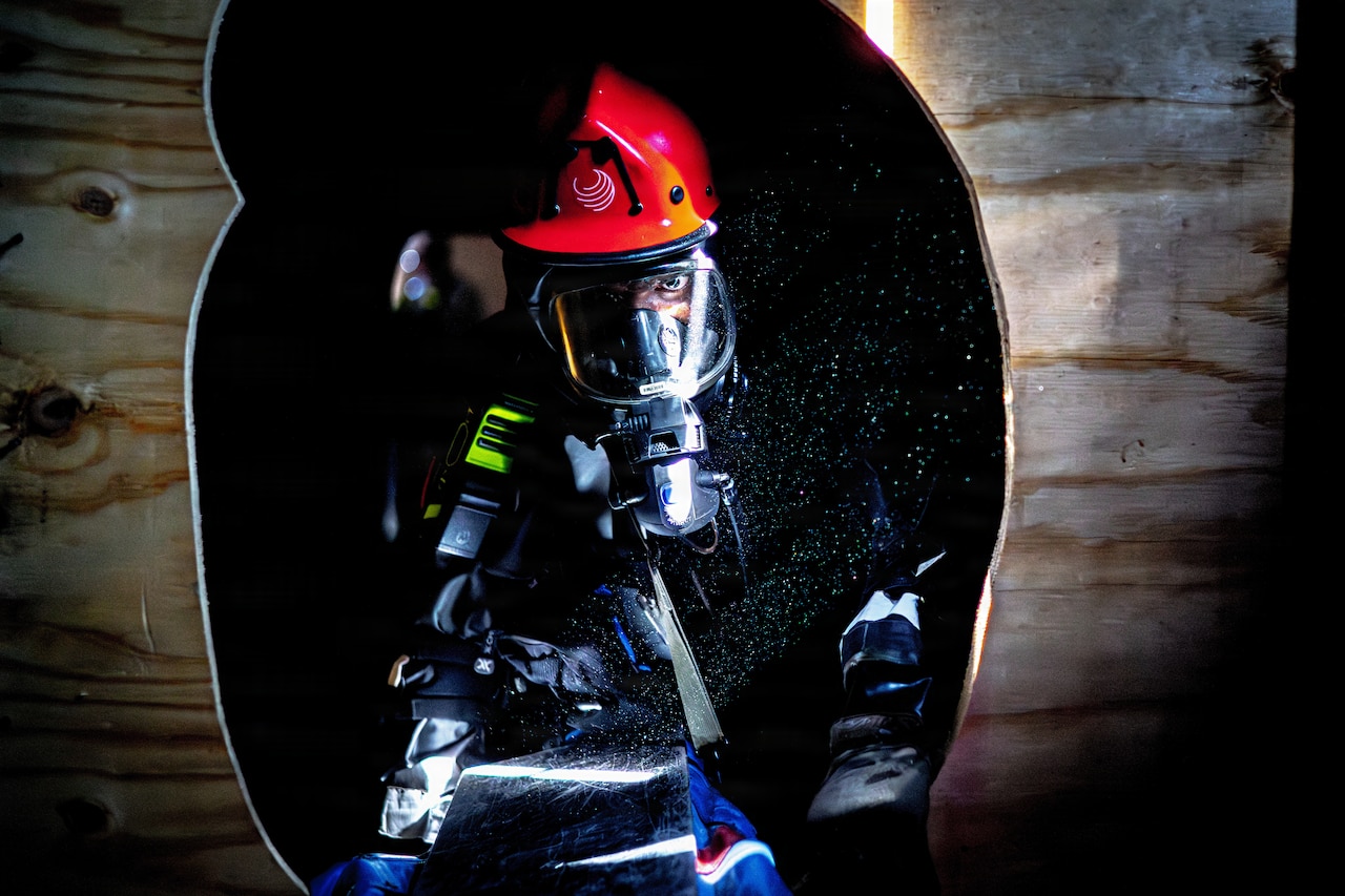 A person dressed in firefighter gear climbs through a dark hole.