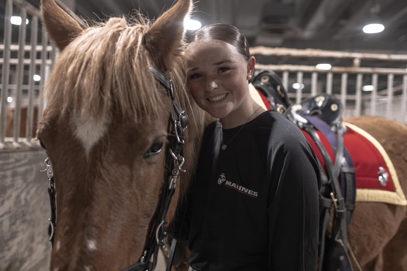 A woman in casual attire smiles as she leans against a horse and poses for a photo.