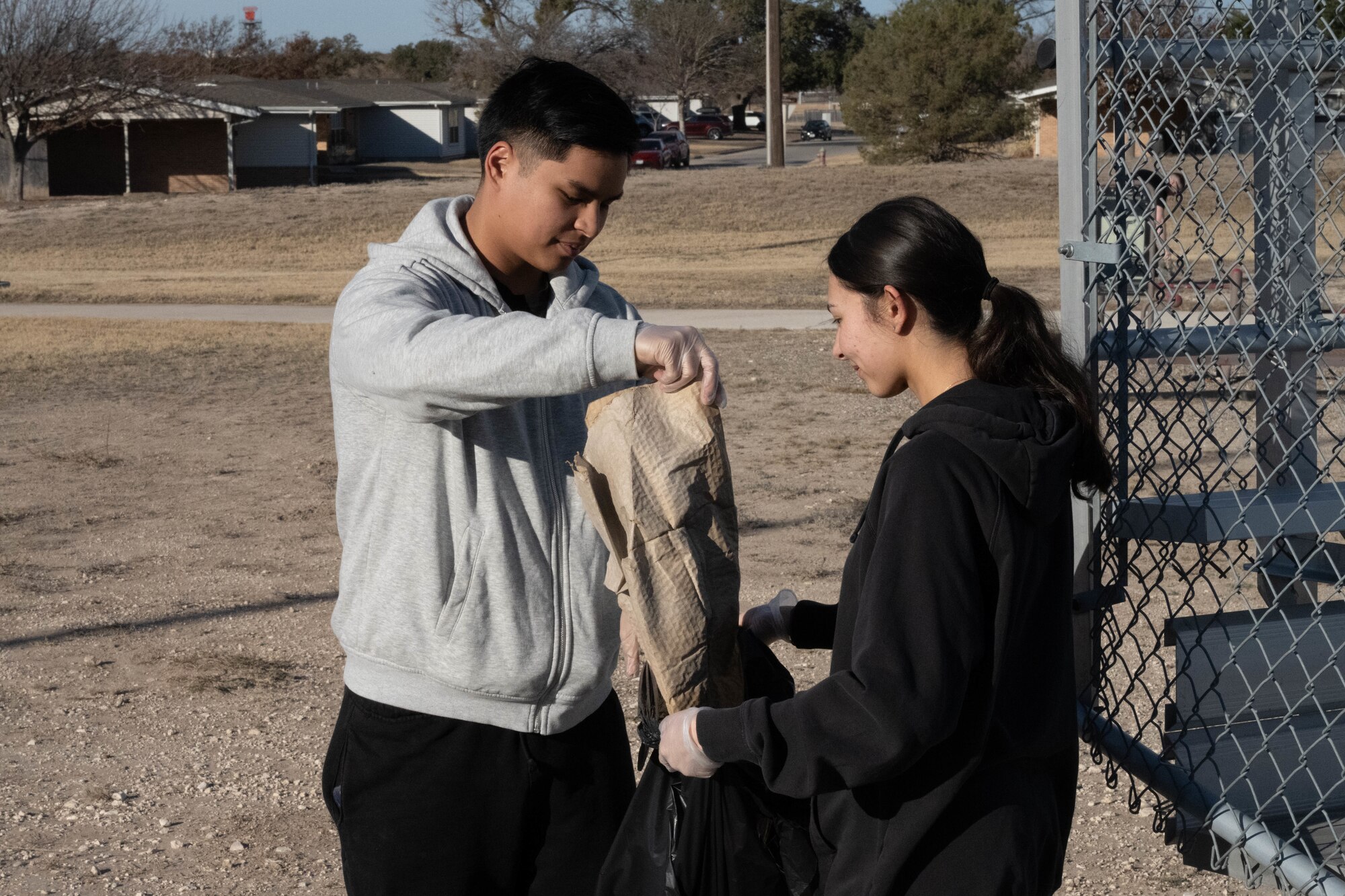 Volunteers from the Laughlin Beautification Team place litter inside a garbage bag at Laughlin Air Force Base, Texas, Feb. 7, 2026. The group collected over 50 pounds of trash during the first cleanup event. (U.S. Air Force photo by Airman 1st Class Darryl Keith)
