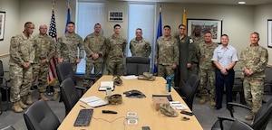 A group of senior leaders stand at the end of a conference table after awarding a junior Airman a performance award.