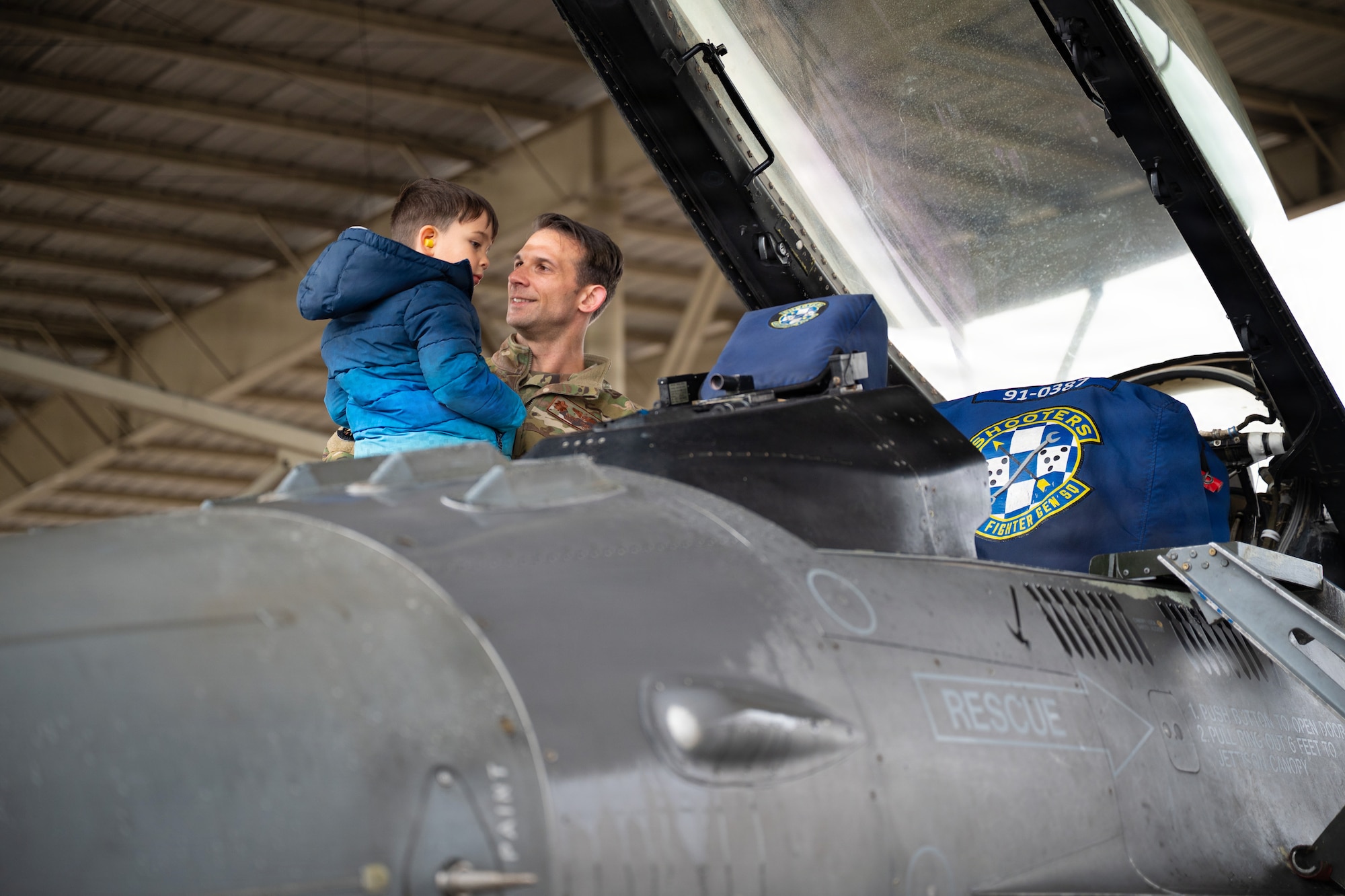 An Airman and his son look inside the cockpit of a fighter jet