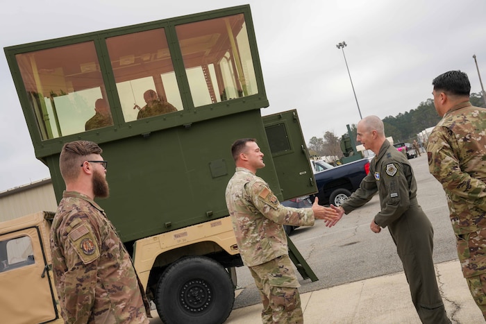 an Airman and the 15th Air Force commander shake hands in front of a mobile air traffic control tower vehicle