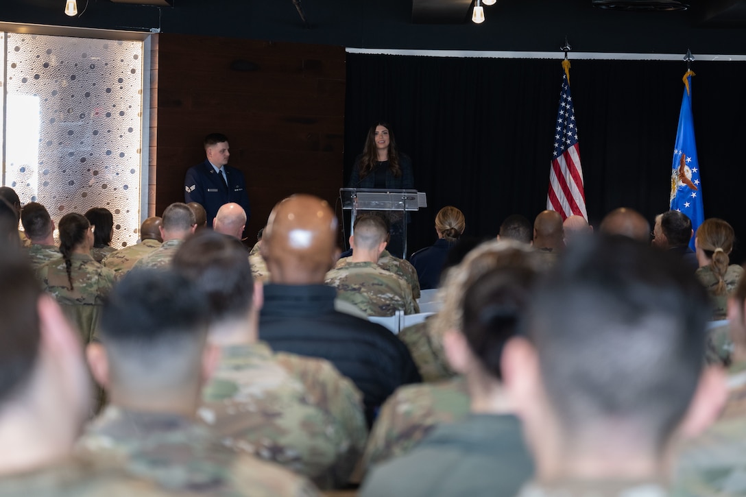 A woman stands at a podium, an audience looks at her.