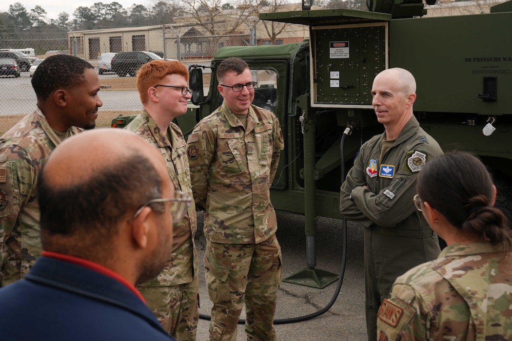 five Airmen stand in a semicircle around a commander as he speaks to them