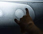 An Airman points at an aircraft panel’s crack, faintly visible on an X-ray scan.