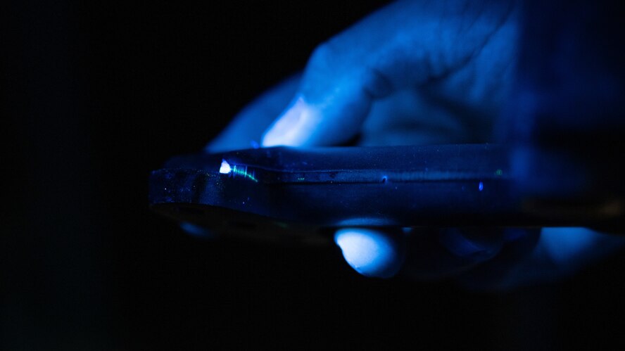 An Airman shines a blacklight on a hydraulic line piece.