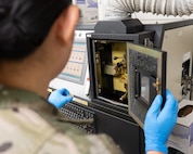 An Airman places a small container of engine oil into an analyzer machine.